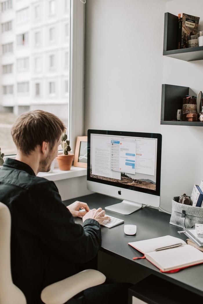 Man working on a desktop computer in an indoor office setting near a window.
